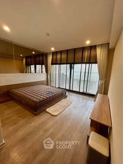 Spacious bedroom with large windows and wooden flooring in modern apartment