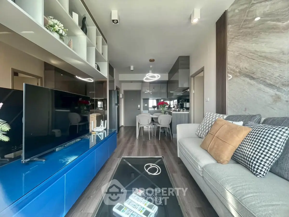 Modern living room with sleek design, featuring a large TV, stylish sofa, and open kitchen layout.