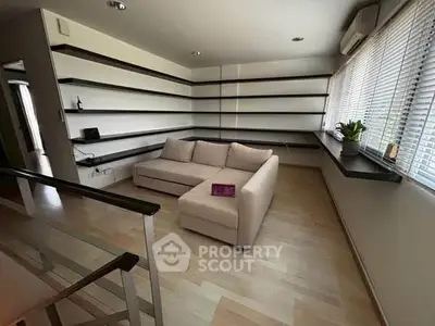 Modern living room with sleek shelving and cozy sectional sofa, featuring large windows for natural light.