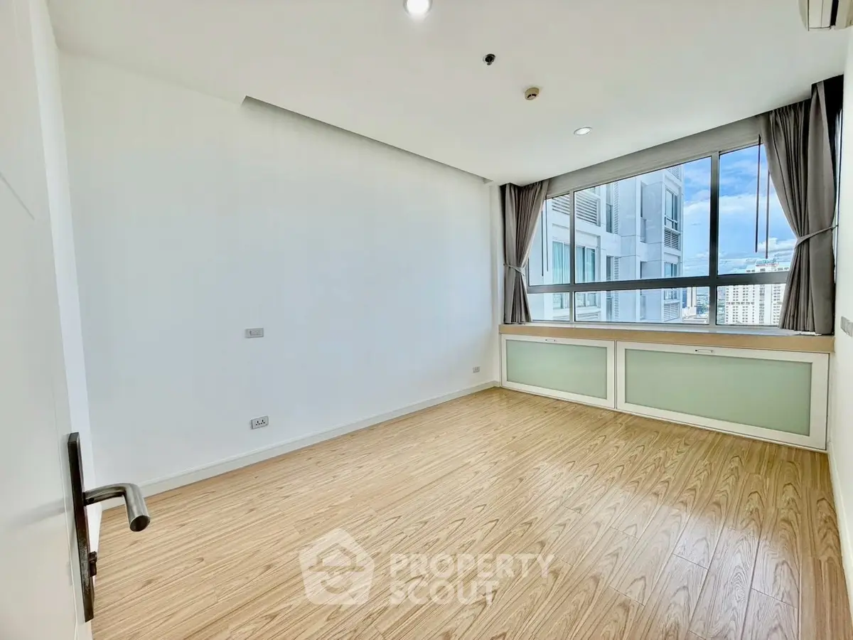 Spacious empty room with large window and wooden flooring in modern apartment