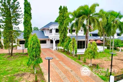 Stunning two-story house with lush garden and palm trees, featuring a spacious driveway and elegant architecture.