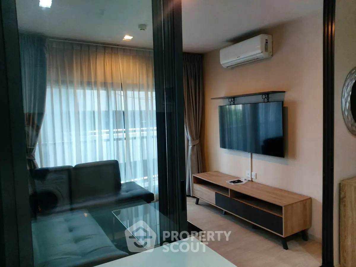 Modern living room with sleek furniture and wall-mounted TV, featuring large windows and air conditioning.