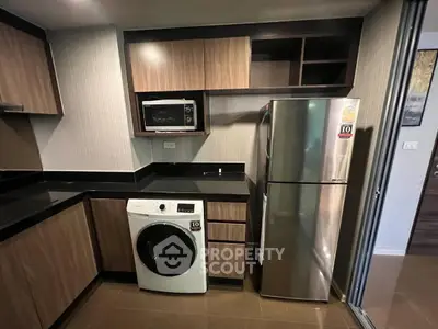 Modern kitchen with sleek appliances and wood cabinetry, featuring a washing machine and microwave.