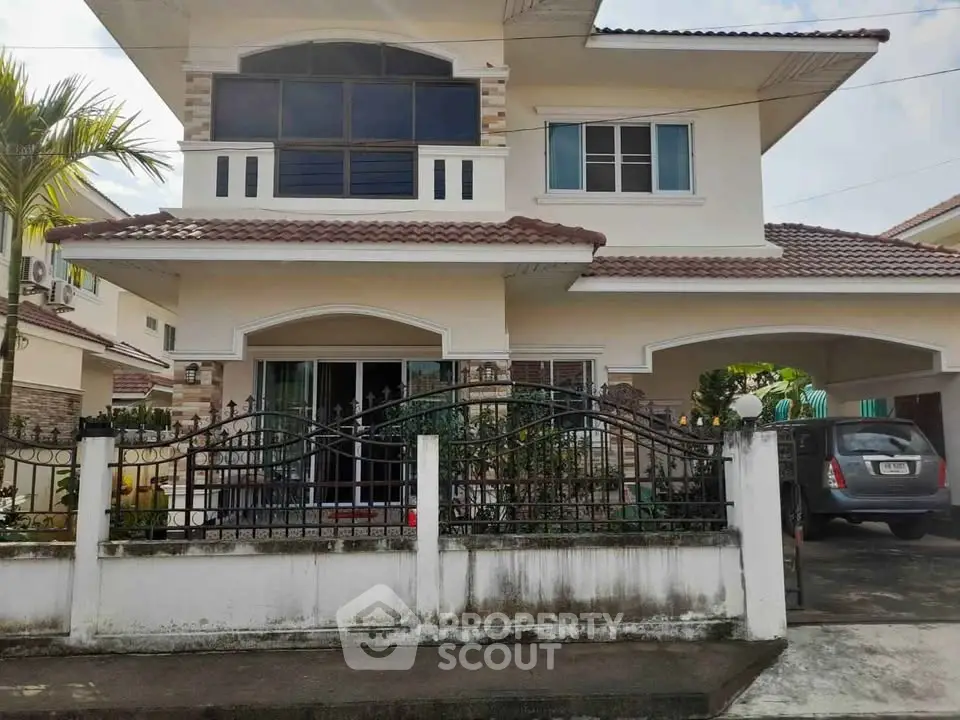 Charming two-story house with a tiled roof, spacious driveway, and lush garden in a serene neighborhood.