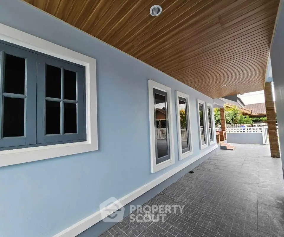 Modern exterior with blue walls and wooden ceiling, showcasing sleek design and spacious walkway.