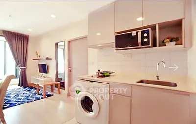 Modern apartment kitchen with washing machine and microwave, open layout to living room with TV and balcony view.