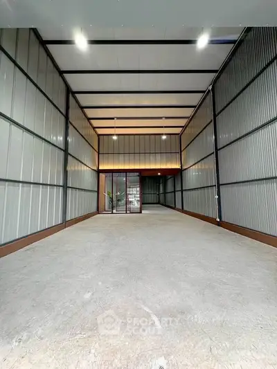 Spacious industrial-style garage with high ceiling and metal walls, perfect for storage or workshop use.