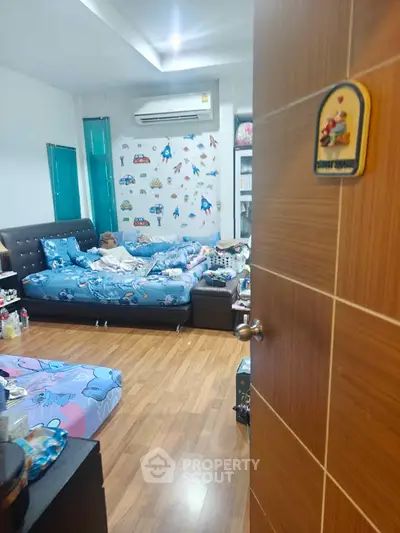 Cozy bedroom with wooden flooring and playful wall decor, featuring a comfortable bed and air conditioning.