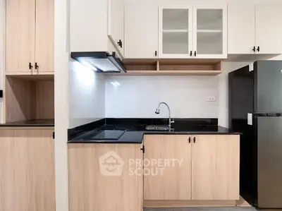 Modern kitchen with sleek black countertops and wooden cabinetry, featuring a built-in stove and spacious fridge.