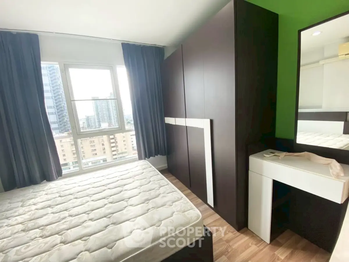 Modern bedroom with large window and city view, featuring sleek wardrobe and vanity desk.