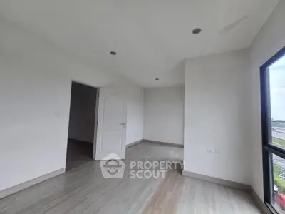 Spacious empty room with large window and wooden flooring, ideal for customization.