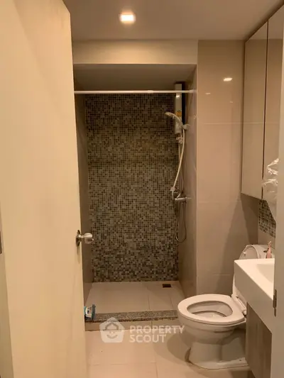 Modern bathroom with a walk-in shower featuring mosaic tiles, a sleek toilet, and a well-lit vanity area, perfect for contemporary living.