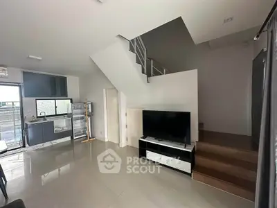 Modern open-plan living room with sleek kitchen and staircase, featuring a minimalist design and natural light.