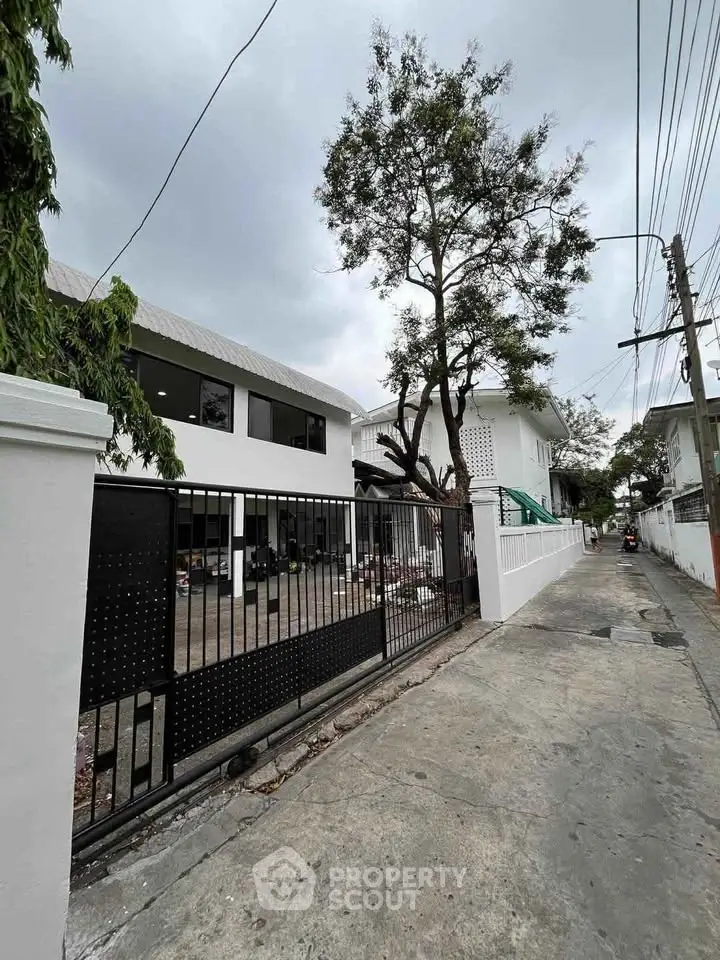 Modern white building with gated entrance and tree-lined street view