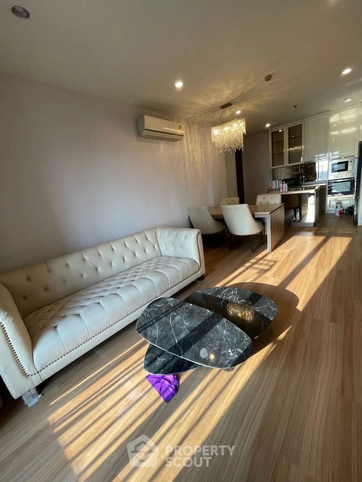 Luxurious living room with elegant sofa and modern dining area, featuring a chic chandelier and stylish decor.