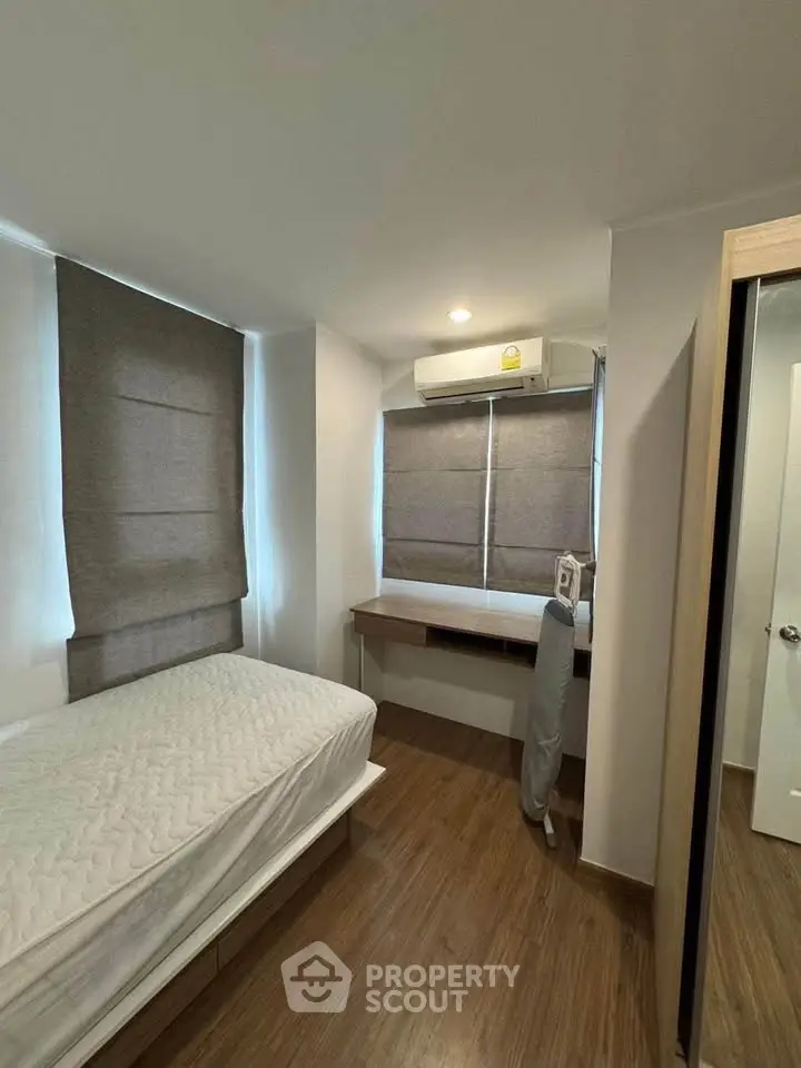 Cozy bedroom with wooden flooring, single bed, and built-in desk under window with blinds.