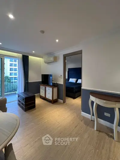 Stylish living room with wooden flooring and modern decor, leading to a cozy bedroom with a balcony view.