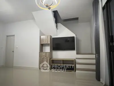 Modern living room with staircase and wall-mounted TV, featuring sleek design and neutral tones.