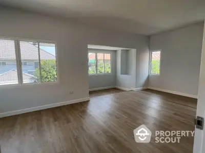 Spacious living room with abundant natural light, hardwood floors, and a serene neighborhood view, perfect for modern living.