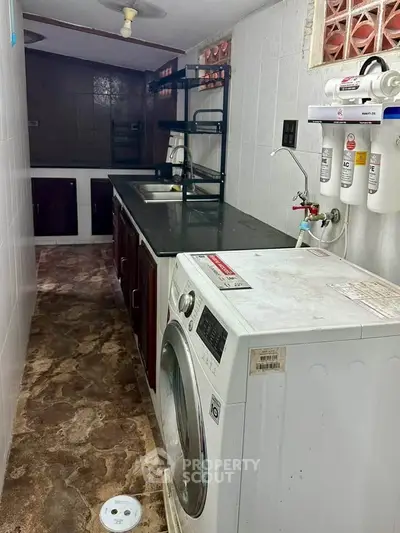 Compact kitchen with washing machine and water filtration system, featuring dark countertops and ample storage.