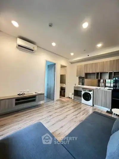 Modern living room with open kitchen and washing machine, featuring sleek wooden cabinetry and cozy seating.