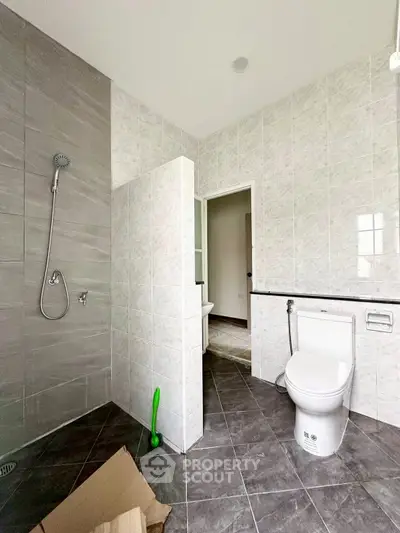 Spacious modern bathroom with tiled walls and floor, featuring a shower and toilet.