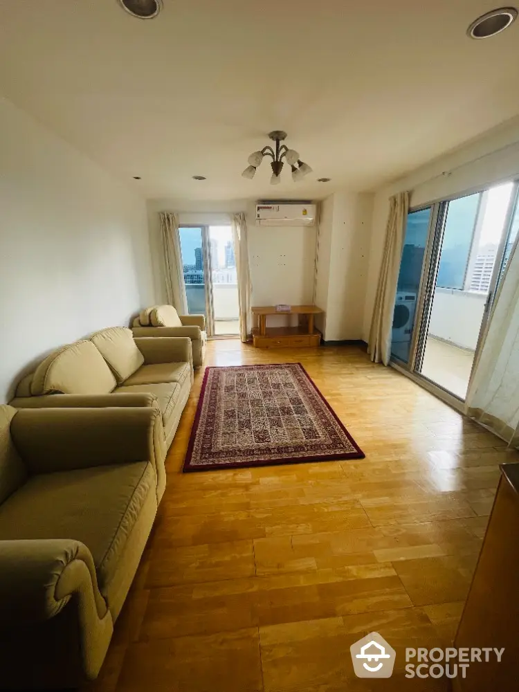 Spacious living room with balcony and city view, featuring cozy sofas and elegant wooden flooring.