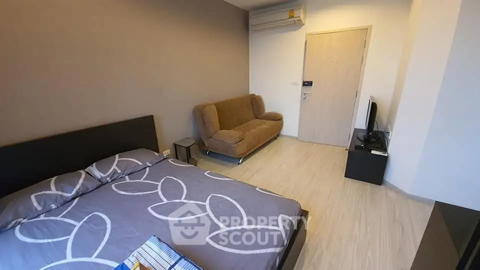Modern bedroom with stylish decor and cozy sofa, featuring a sleek TV setup and air conditioning.