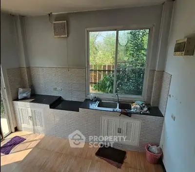 Spacious kitchen with large window and modern countertops, offering a serene garden view.