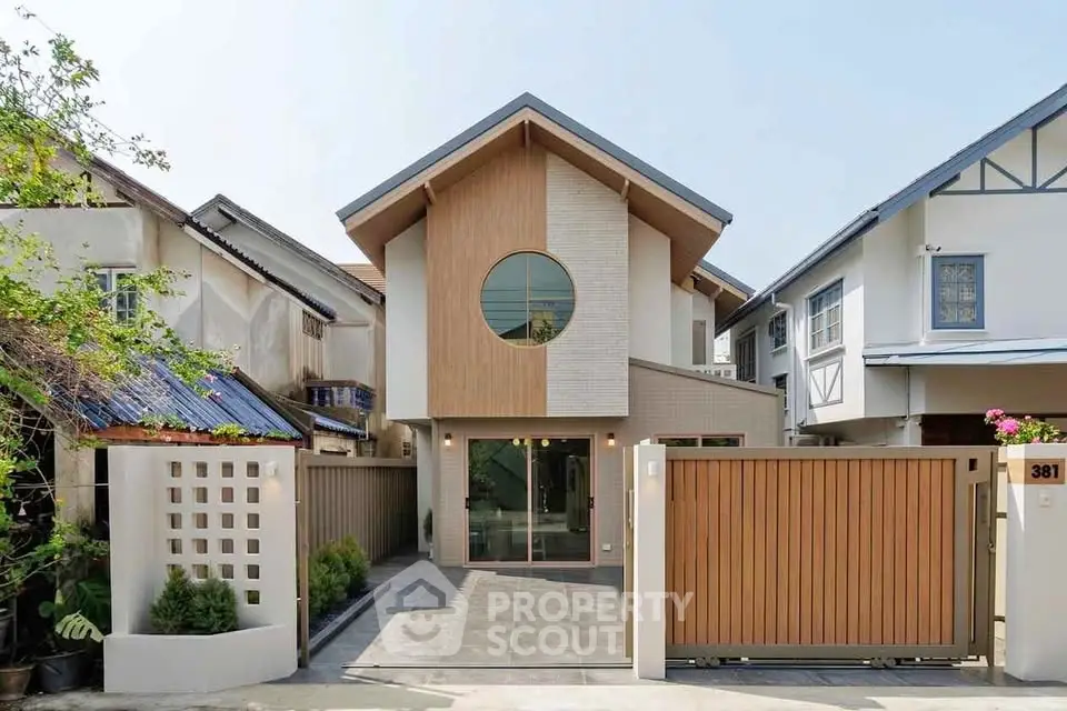 Modern two-story house with unique circular window and wooden gate in a suburban neighborhood.