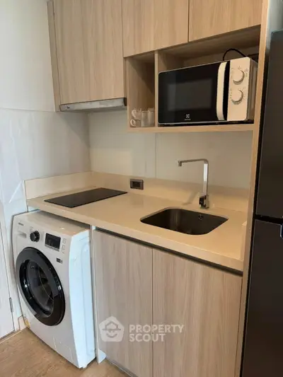 Modern compact kitchen with washing machine, microwave, and sleek cabinetry