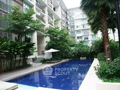Luxurious condominium with a stunning pool surrounded by lush greenery and modern architecture.