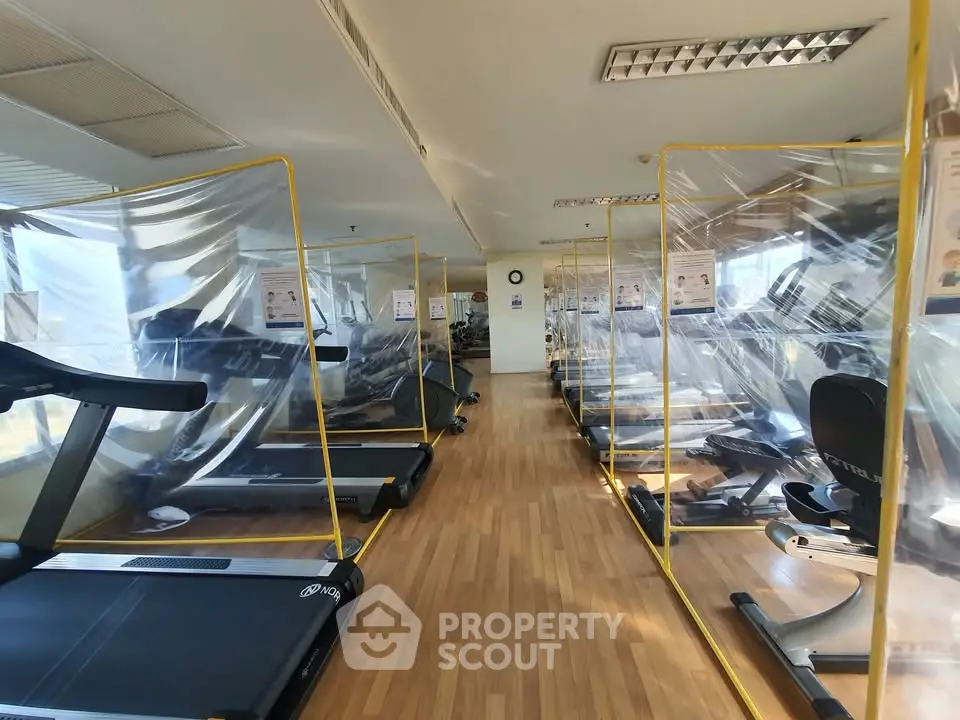 Spacious gym with modern equipment and safety partitions in a luxury apartment complex.