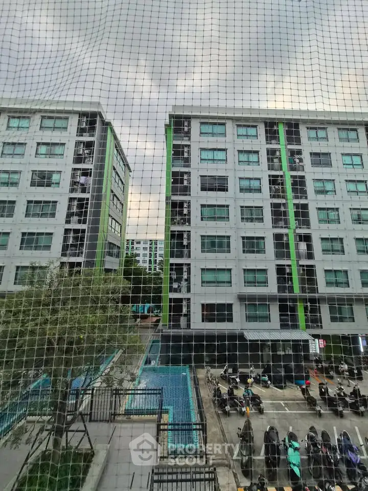 Modern apartment buildings with parking and pool view through safety netting.
