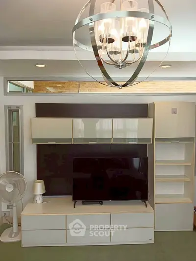 Modern living room with stylish chandelier and sleek entertainment center.