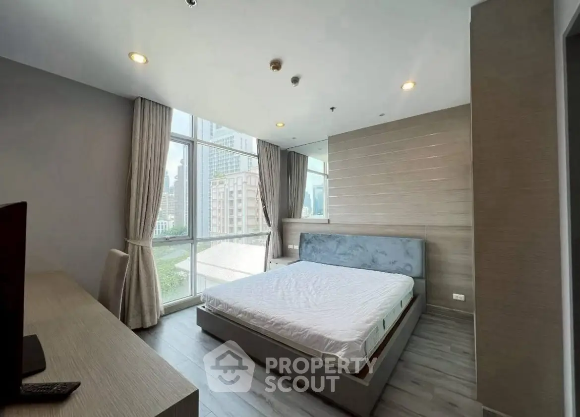 Spacious modern bedroom with large windows and city view, featuring elegant decor and natural light.