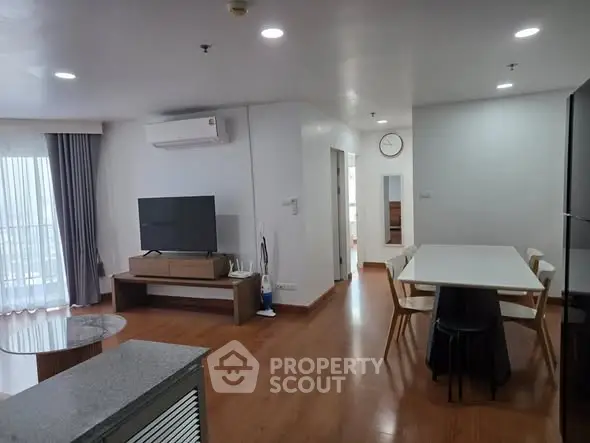 Spacious modern living room with dining area and large TV, featuring sleek wooden flooring and natural light.