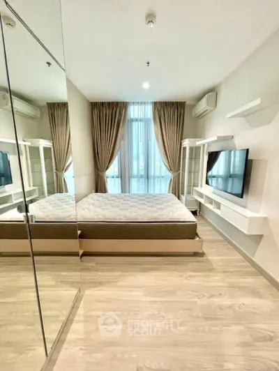 Modern bedroom with mirrored closet and large window, featuring sleek design and natural light.