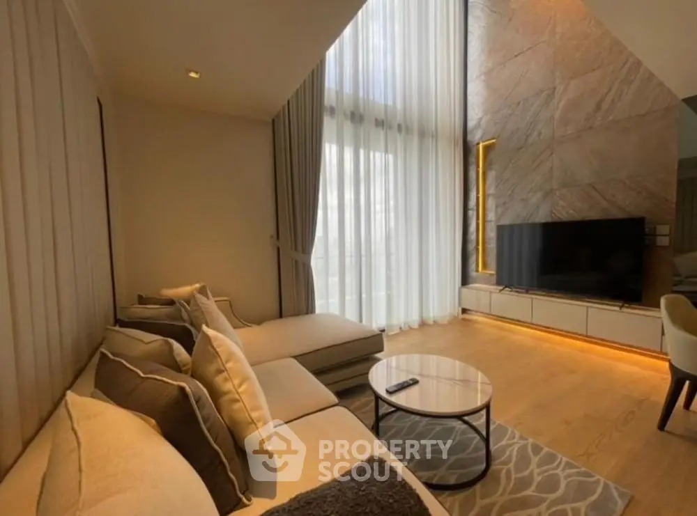 Luxurious living room with high ceilings and modern decor, featuring a large TV and elegant furniture.