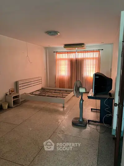 Spacious bedroom with natural light, featuring a bed frame, fan, and TV for comfortable living.