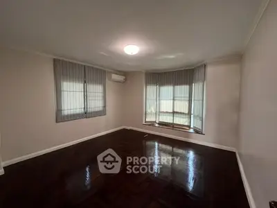 Spacious empty room with wooden flooring and large windows, ideal for customization.