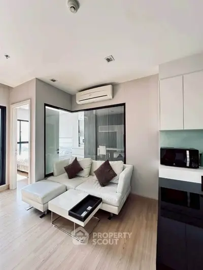 Modern living room with sleek design, featuring a cozy white sofa, stylish decor, and open kitchen layout.
