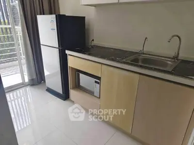 Modern kitchen with sleek appliances and natural light, featuring a fridge and microwave.