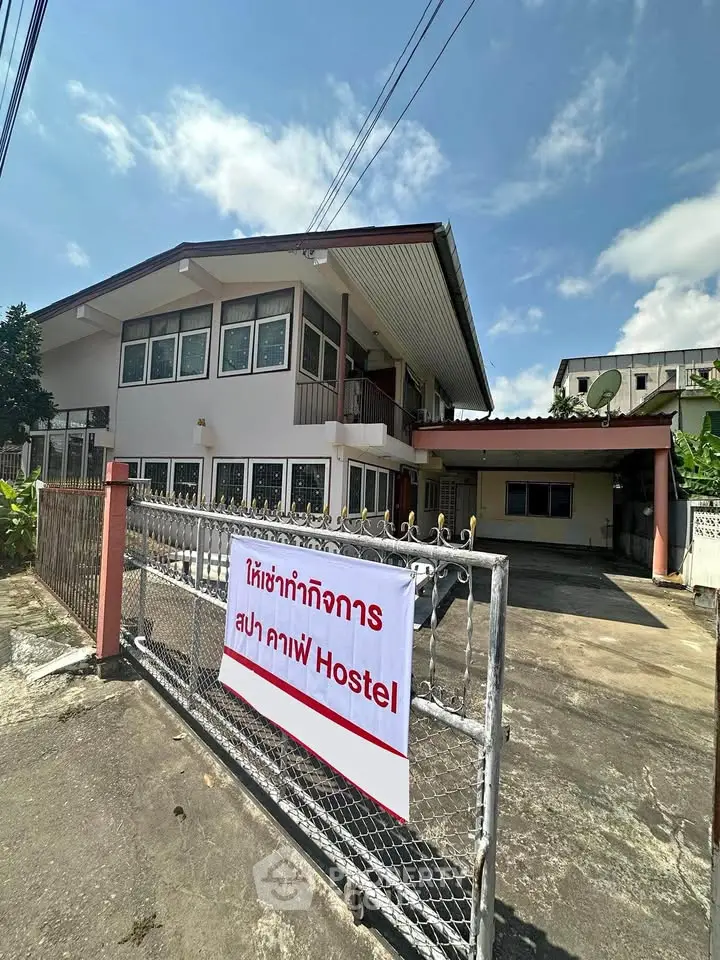 Charming two-story hostel with spacious parking and inviting entrance in sunny urban setting.