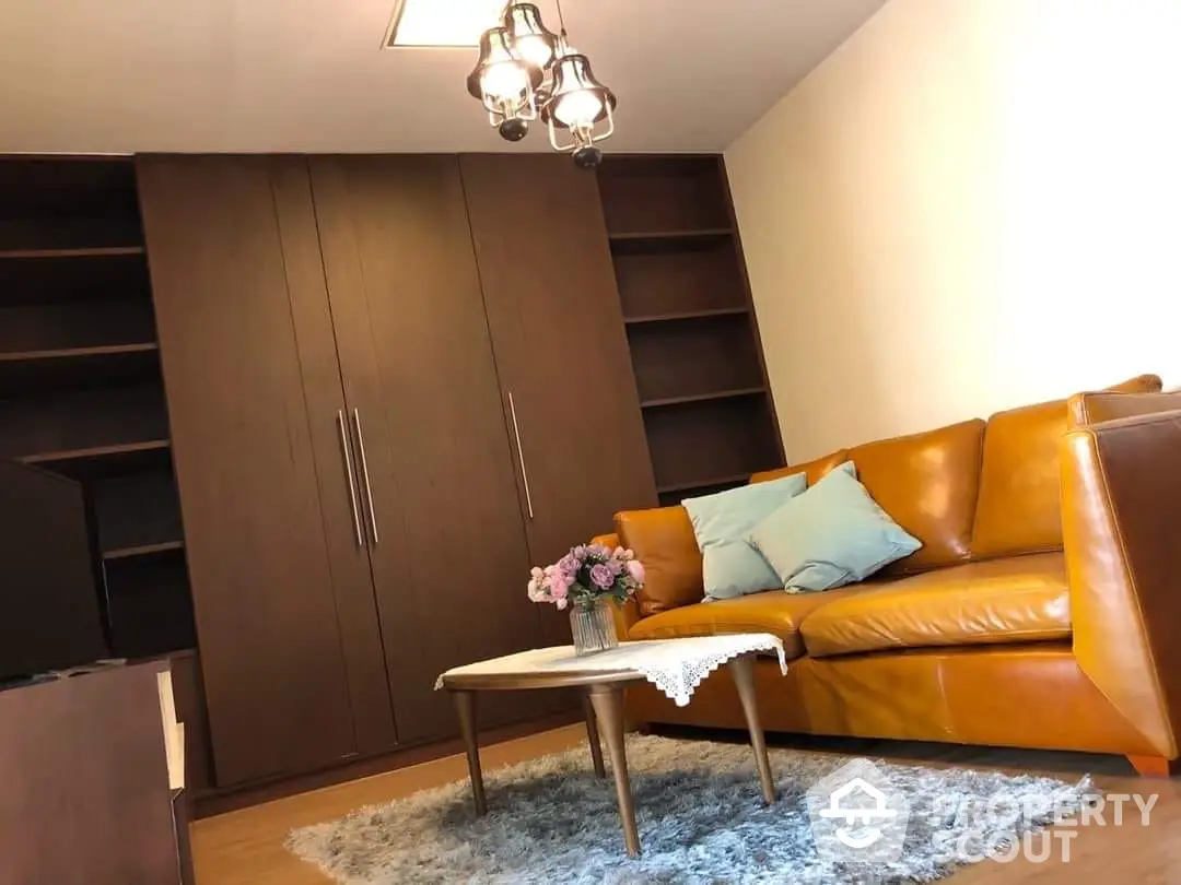 Cozy living space featuring a plush caramel leather sofa, chic glass pendant light, and a sleek dark wood bookshelf, perfect for relaxation.