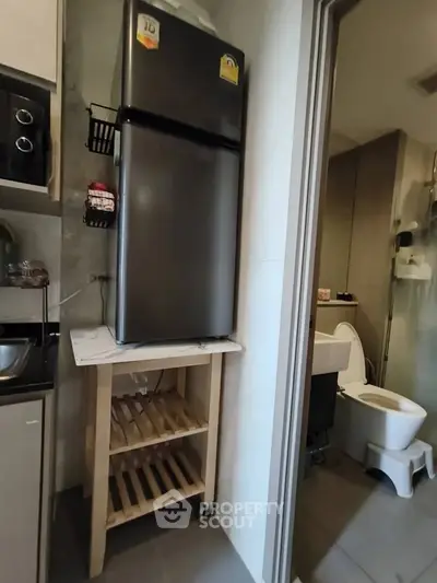 Compact kitchen with fridge and bathroom view in modern apartment