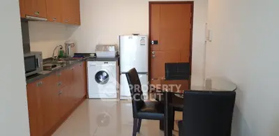 Modern kitchen with wooden cabinets, washing machine, and dining area in cozy apartment.