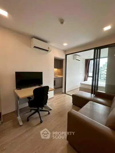 Modern apartment interior with study area and cozy living room, featuring wooden flooring and air conditioning.