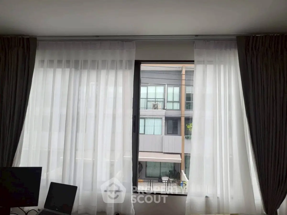Modern apartment window view with elegant curtains and cityscape backdrop.