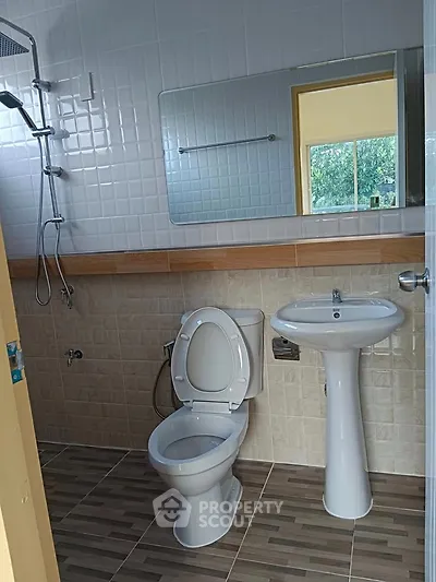 Modern bathroom with sleek fixtures and large mirror, featuring a shower and pedestal sink.